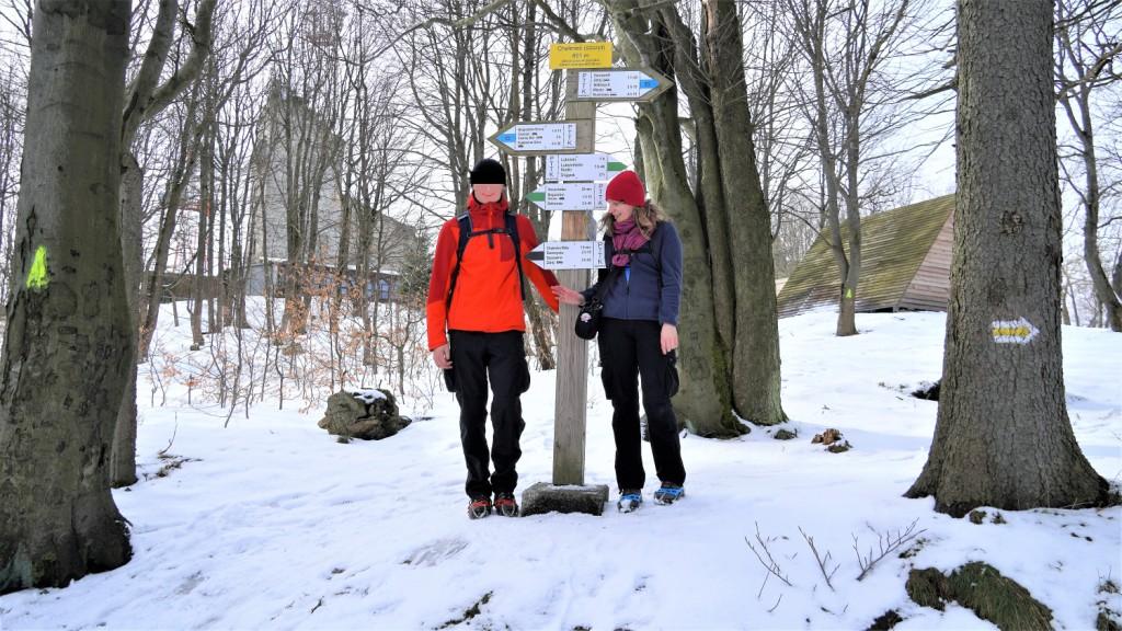 Dwoje ludzi przy słupie z tabliczką informującą o szczycie Chełmca i drogowskazami szlaków zielonego i niebieskiego